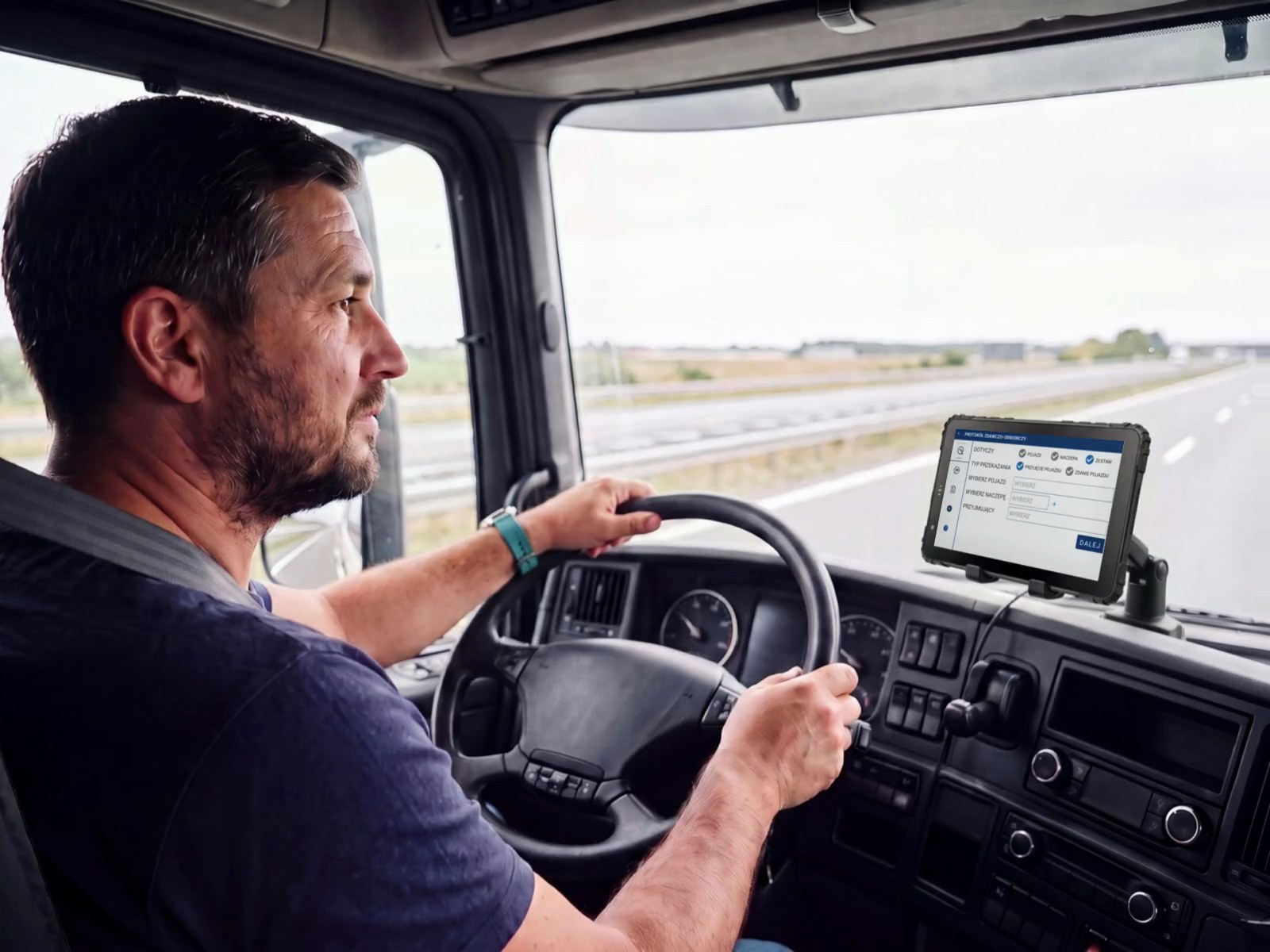 Kierowca ciężarówki na autostradzie, obie ręce na kierownicy, wzrok na drodze. Na desce rozdzielczej terminal w uchwycie z ekranem protokołu zdawczo-odbiorczego w aplikacji frameLOGIC