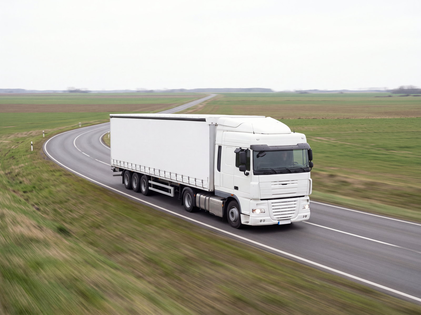 A single white tractor-trailer travelling along a country road that curves away across open fields